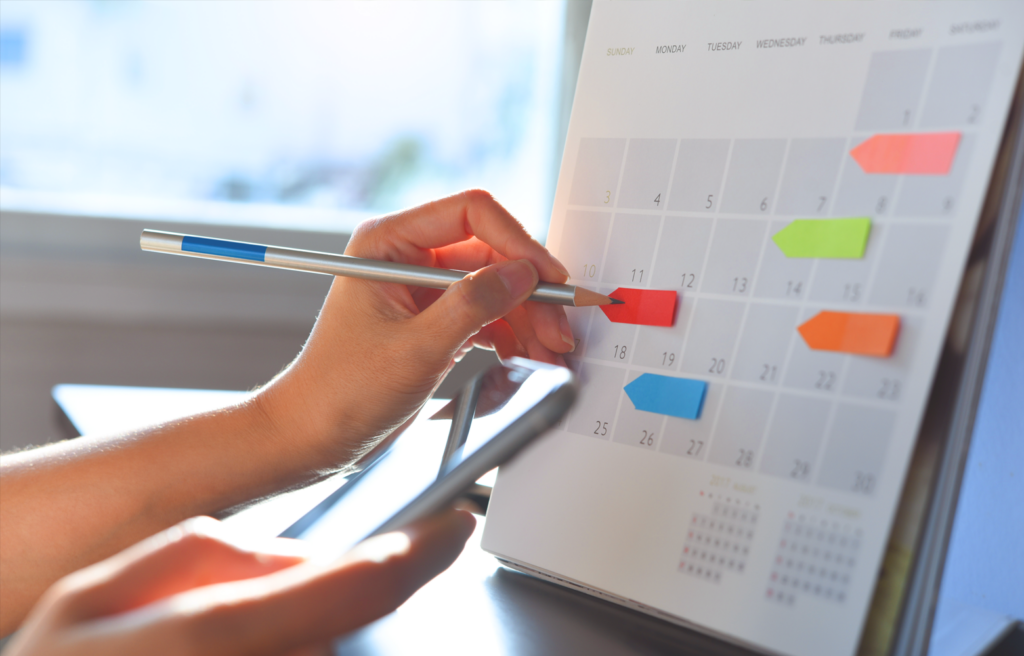 Mão segurando uma caneta e marcando datas em um calendário, representando o planejamento estratégico do calendário comercial no marketing digital.