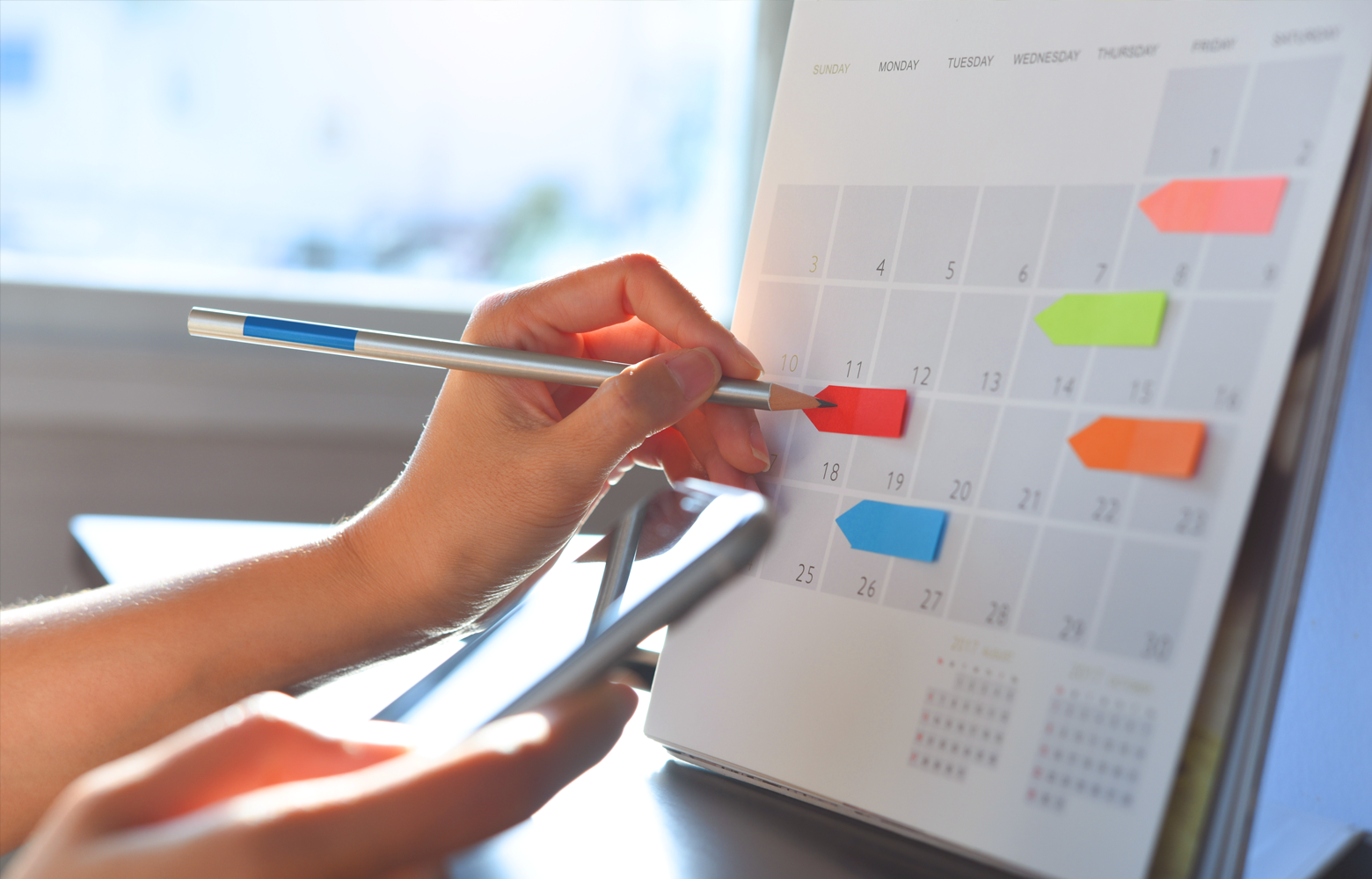 Mão segurando uma caneta e marcando datas em um calendário, representando o planejamento estratégico do calendário comercial no marketing digital.