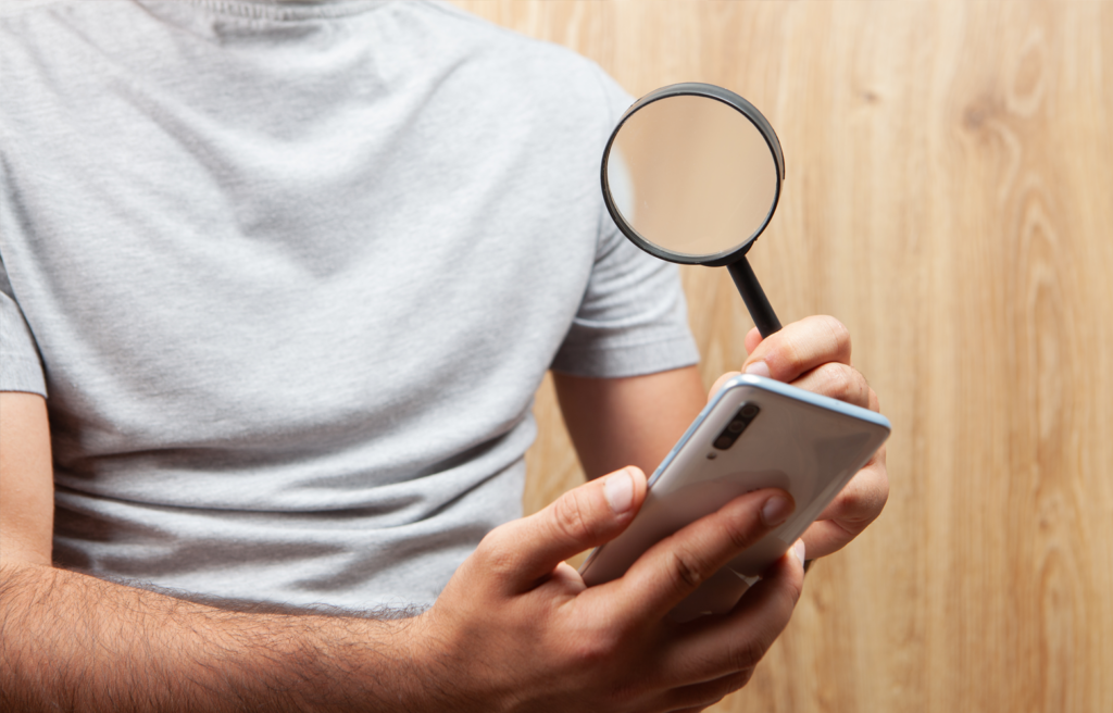 Pessoa segurando um smartphone enquanto observa a tela com uma lupa, representando análise e intenção de busca no ambiente digital.