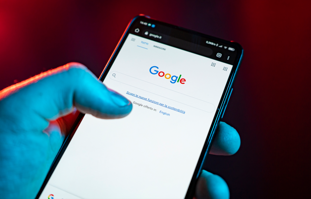 Pessoa utilizando o celular com a página inicial do Google aberta, realizando uma busca online, representando a interação do cliente com o SEO.