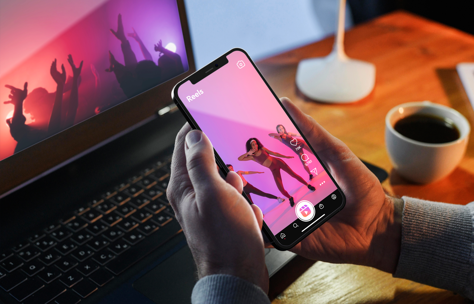 Pessoa segurando um smartphone com um vídeo curto, recomendado pelo algoritmo, do Instagram, em reprodução, enquanto um notebook aparece ao fundo exibindo conteúdo digital.