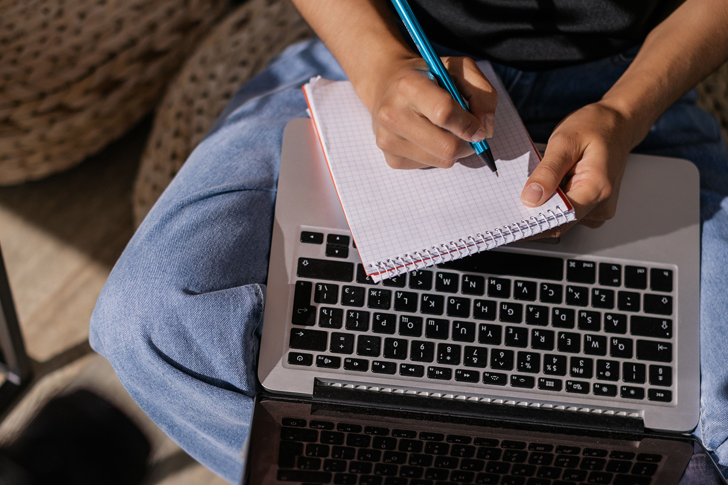 Pessoa escrevendo ideias de conteúdo em um caderno sobre um notebook.